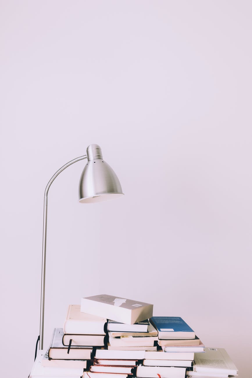 silver desk lamp near pile of books